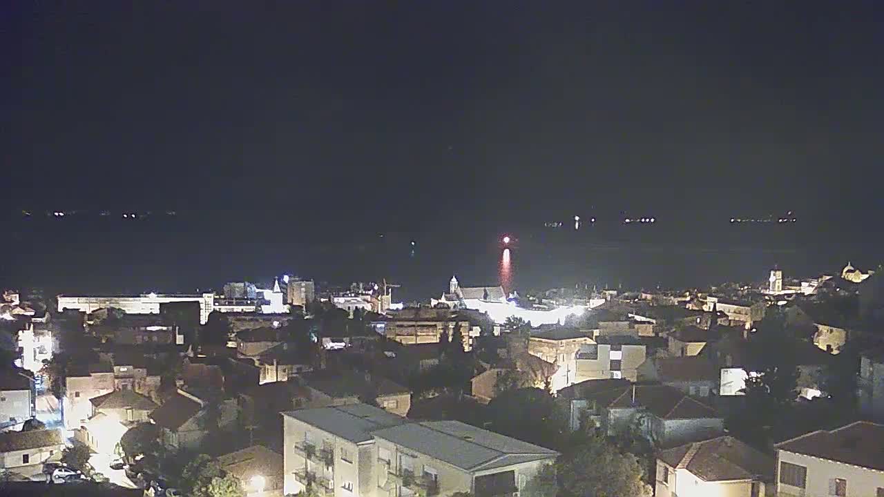 A nighttime, aerial view of a coastal town illuminated with lights, overlooking a dark body of water.