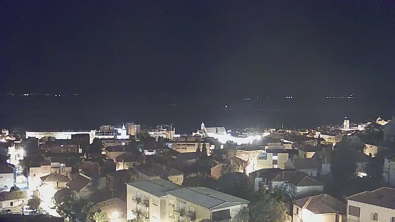A nighttime view of a coastal town illuminated by streetlights, overlooking a dark body of water under a clear sky.
