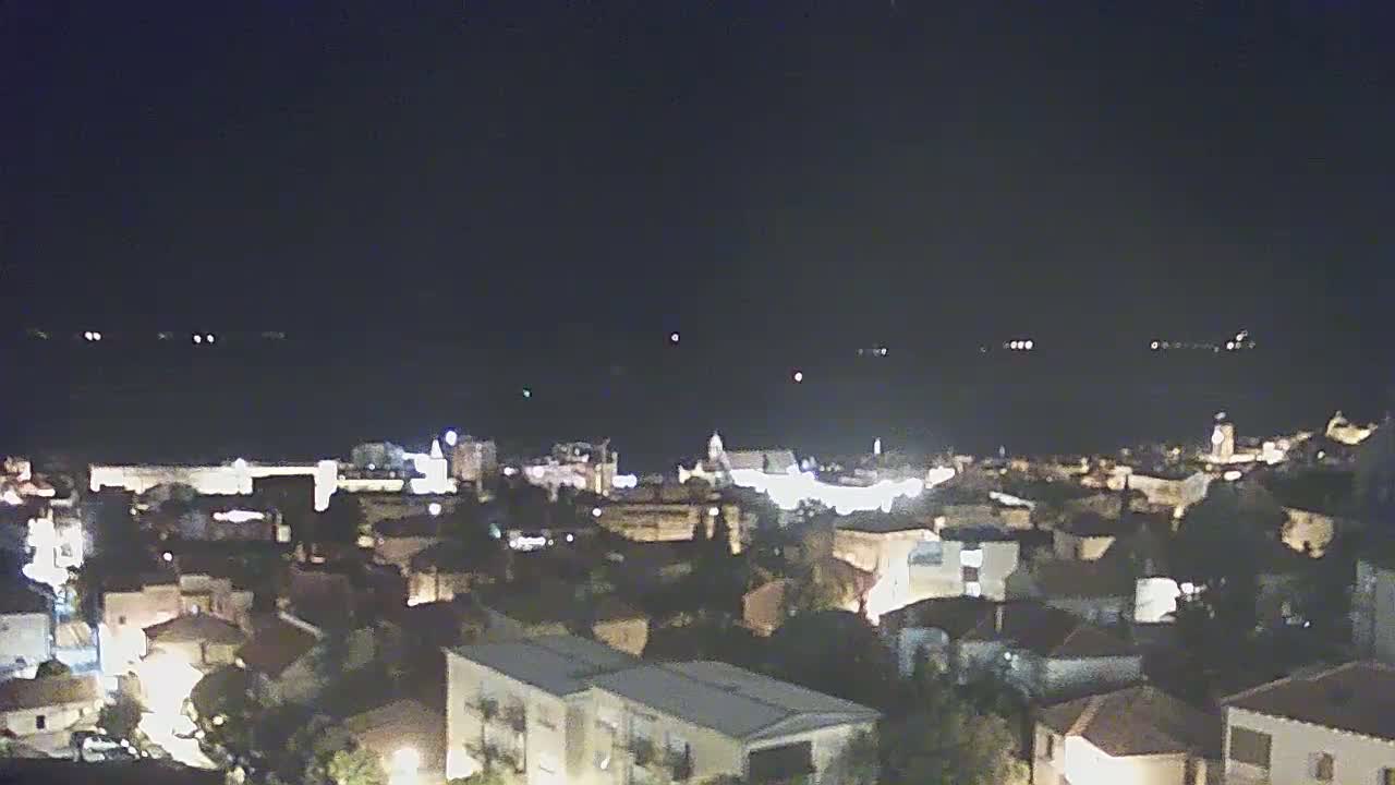 A nighttime, high-angle view of a coastal town with its lights illuminated against a dark sky.