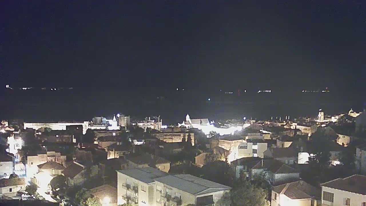 A nighttime, aerial view of a coastal town with its lights illuminated against a dark body of water.