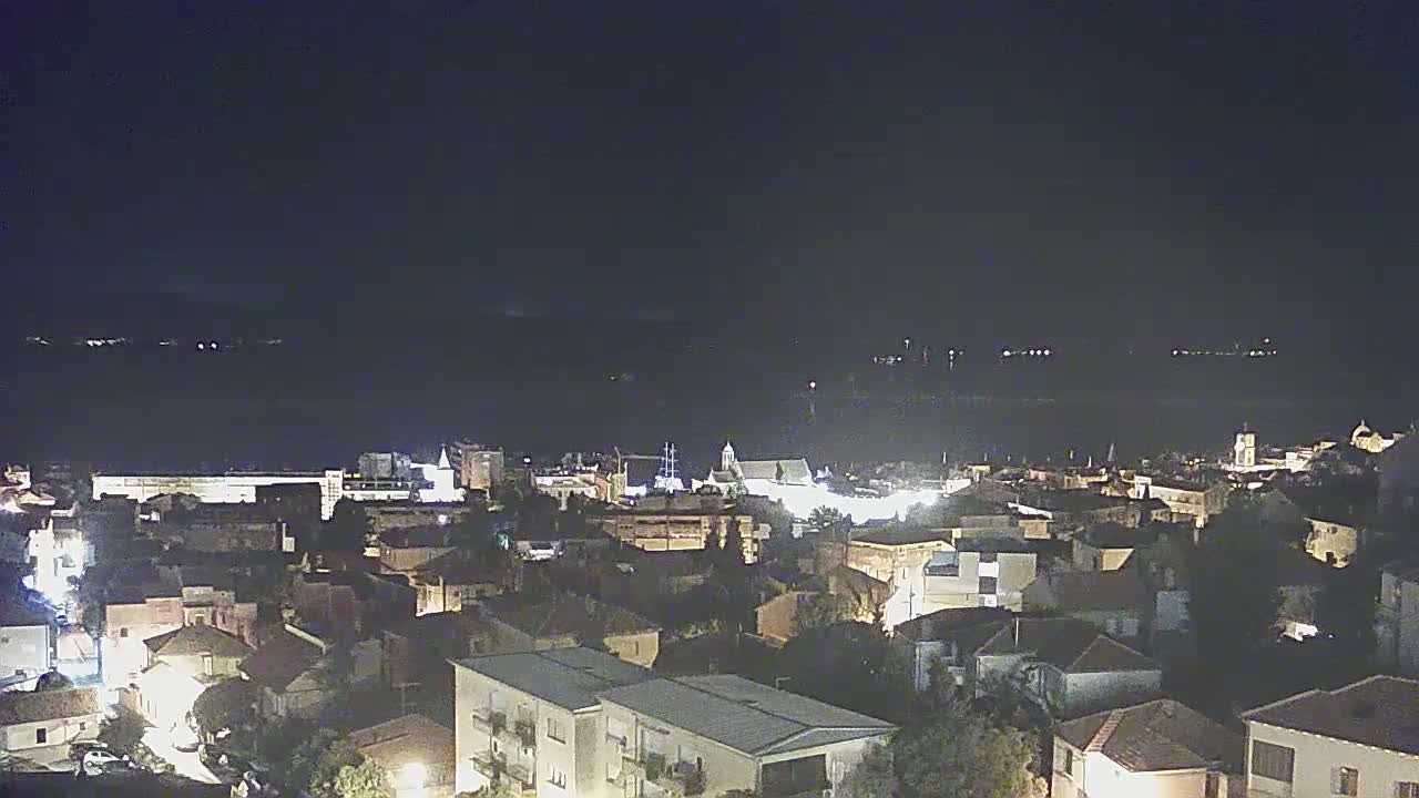 A nighttime, aerial view of a coastal town with its lights illuminated against a dark sea.