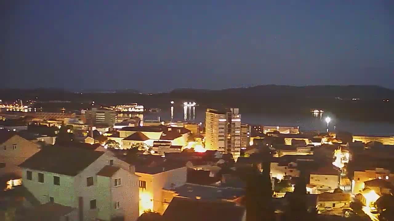 A nighttime view of a coastal town with its lights illuminated, under a dark, clear sky.
