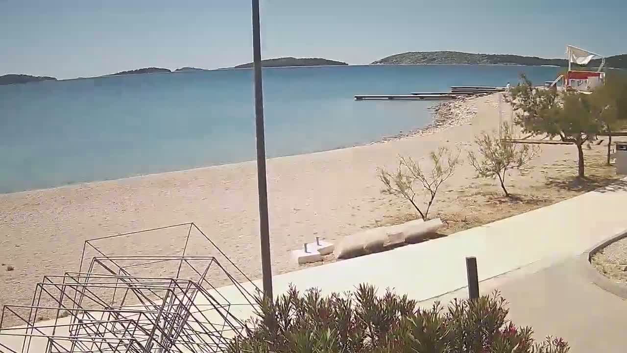 A sandy beach with calm, light blue water stretches to islands in the distance on a sunny day.