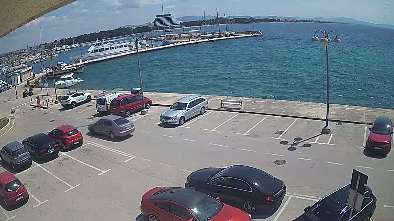 A sunny day overlooking a harbor filled with boats and a parking lot with several cars parked.