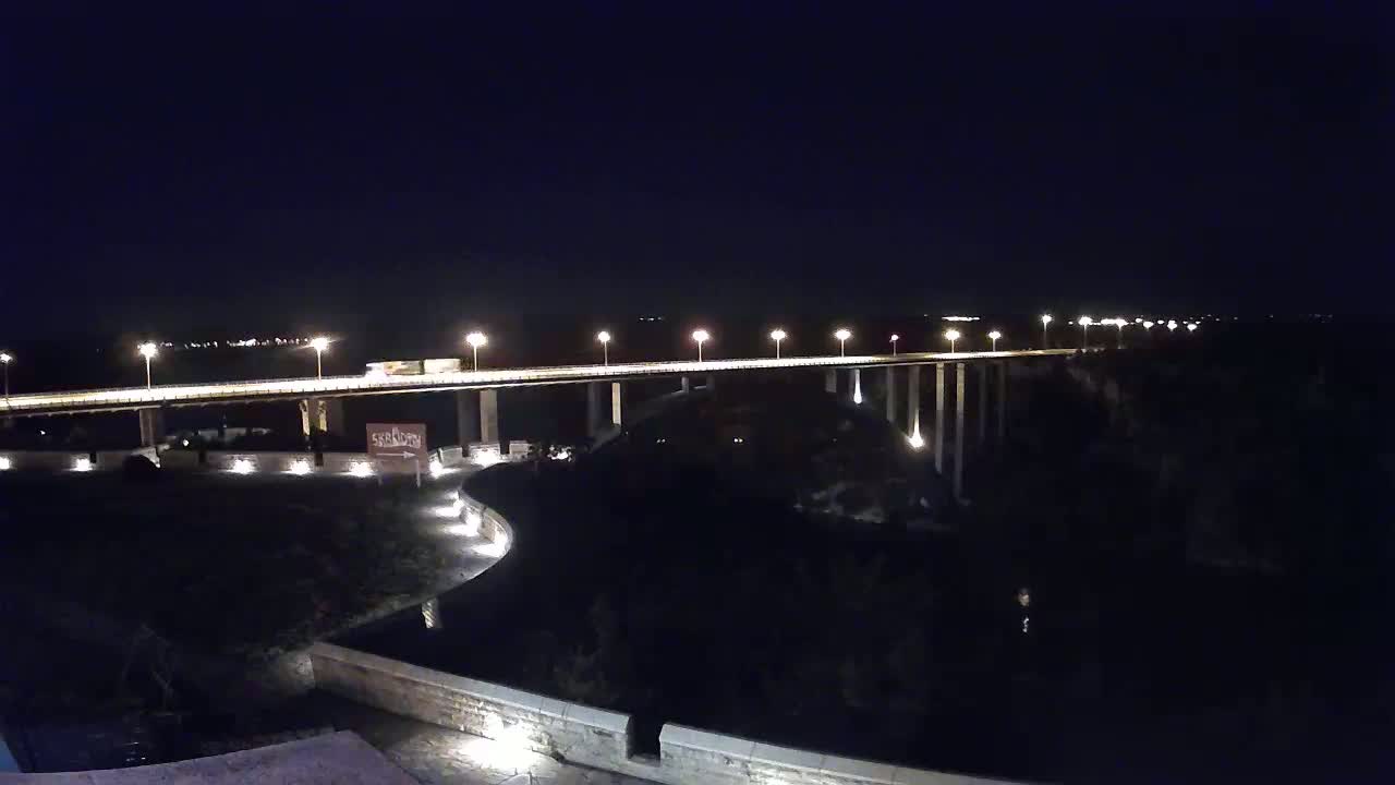 A long, illuminated bridge spans a dark body of water at night.