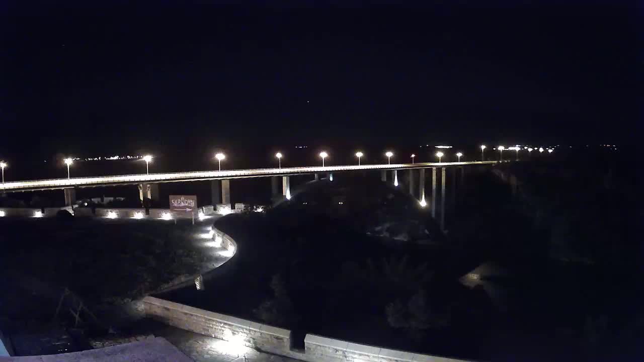 A long, illuminated bridge stretches across a dark body of water at night.