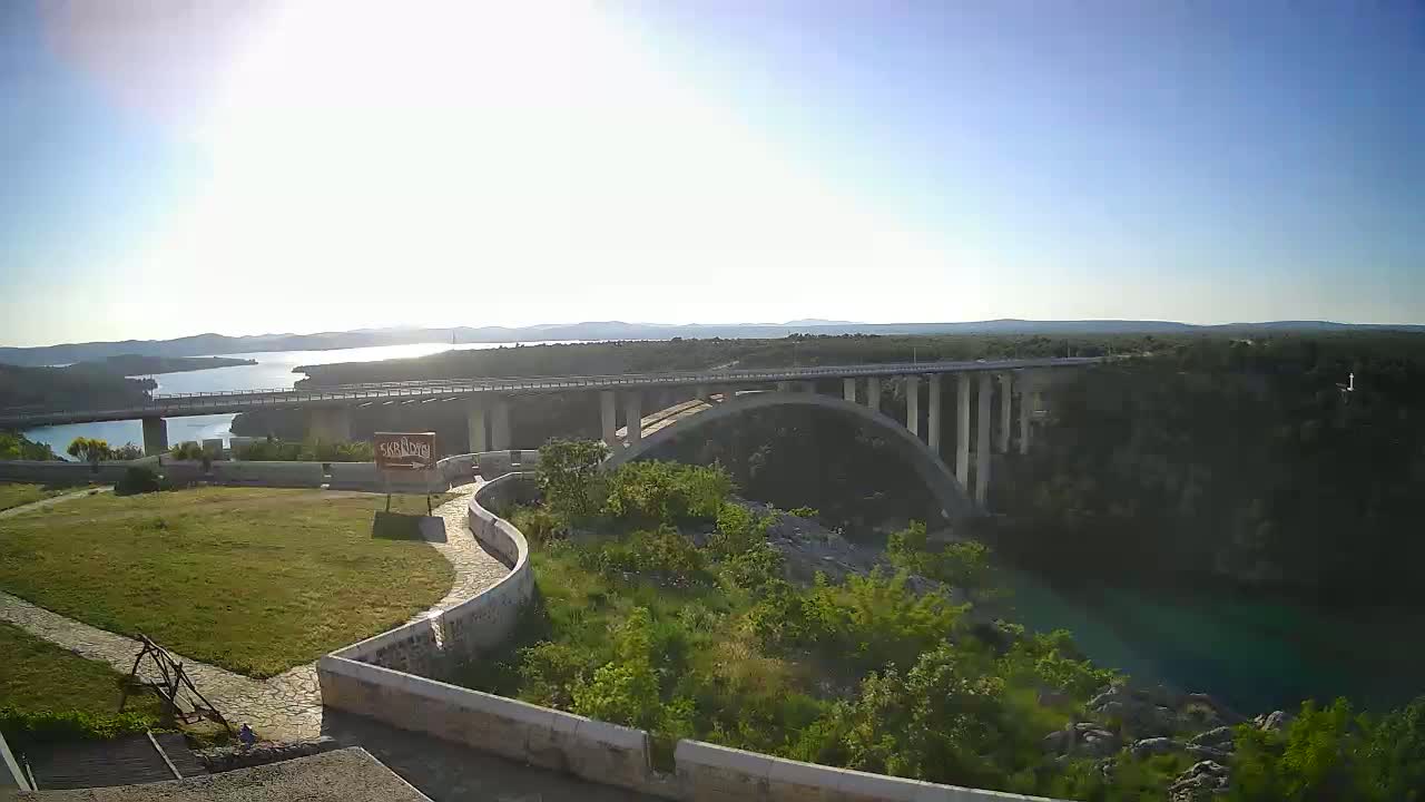 A long, double-decker bridge spans a river valley under a bright, sunny sky.