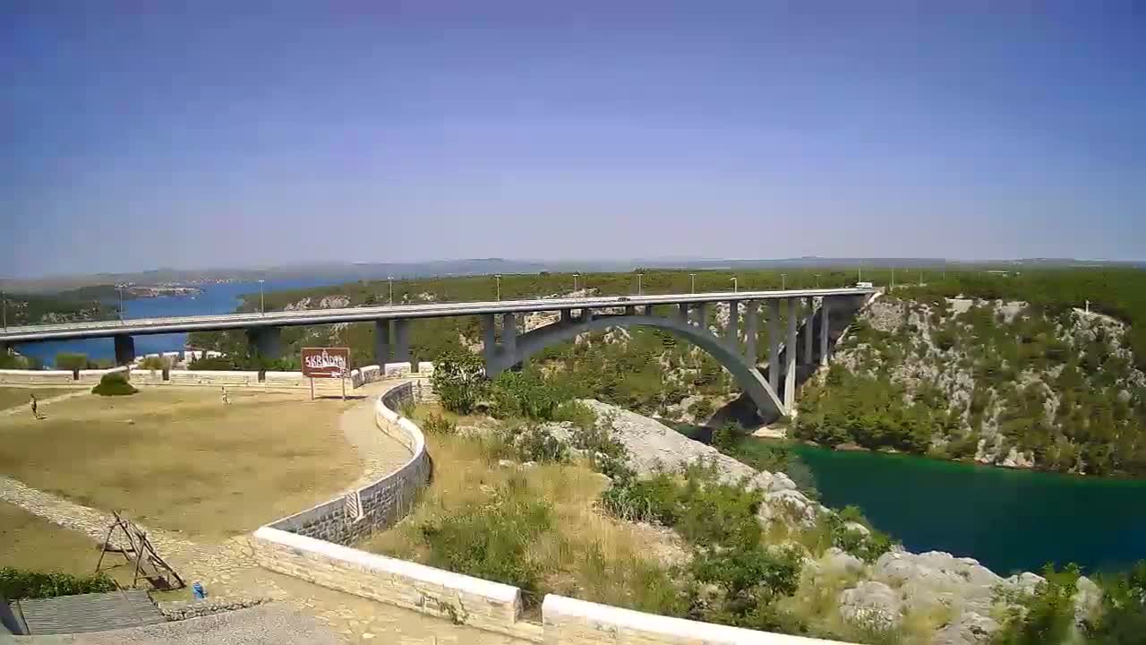 A long bridge arches over a green river valley on a sunny day.