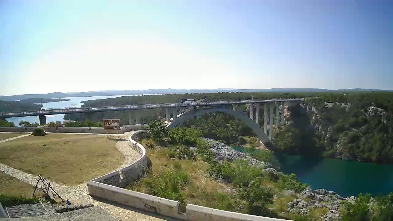A long bridge spans a deep, turquoise river gorge under a clear, sunny sky.