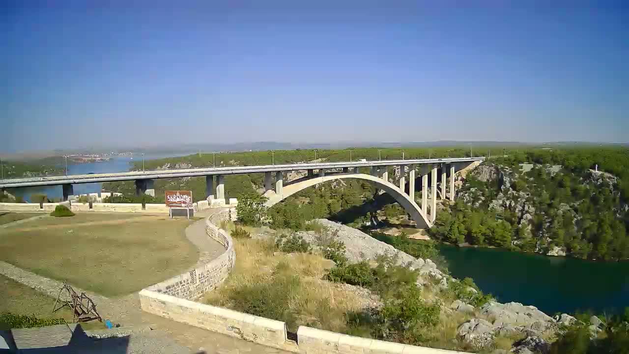 A long concrete bridge spans a deep blue river under a clear blue sky.
