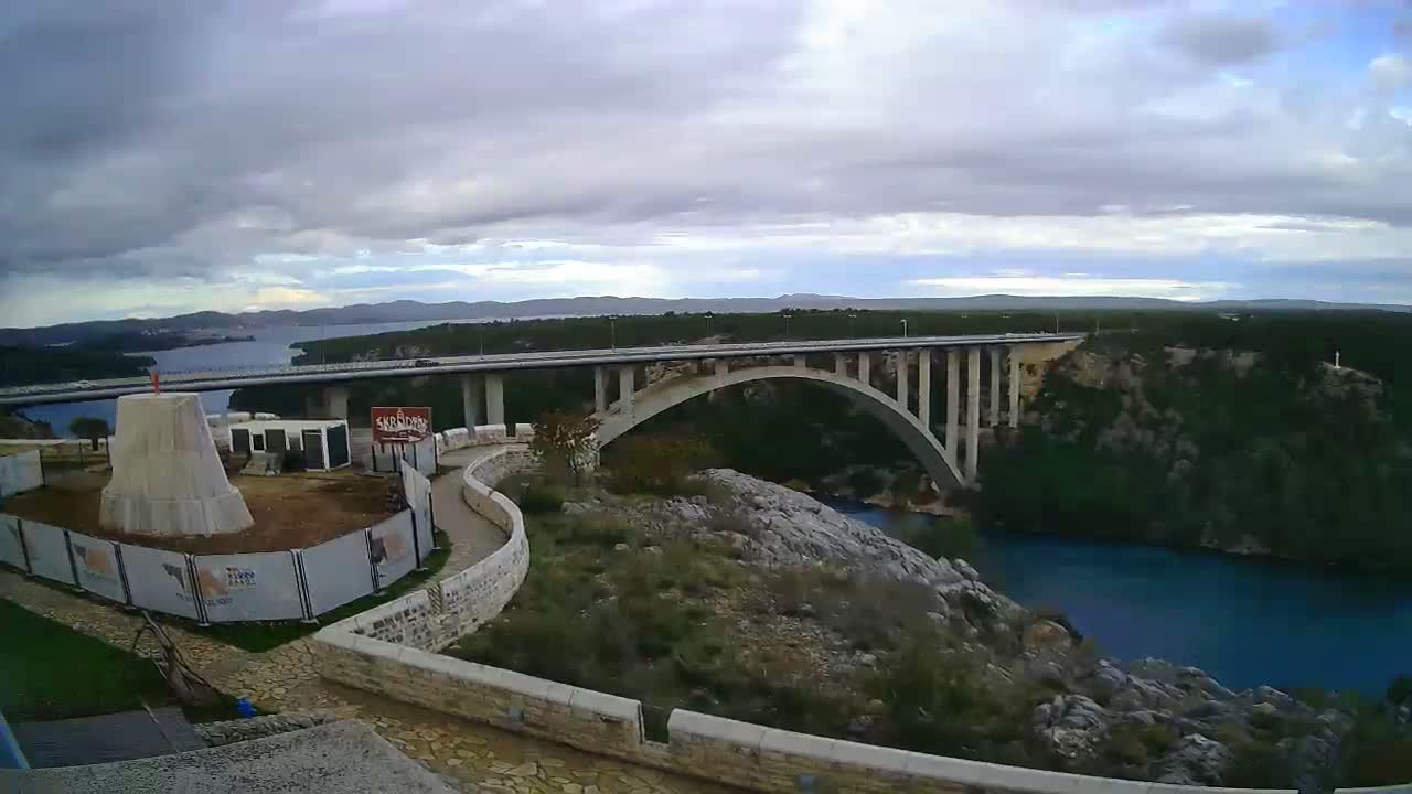 A long concrete bridge spans a deep blue river under a clear blue sky.
