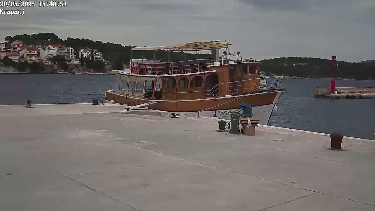 A large wooden passenger boat is docked at a concrete pier on a cloudy day.