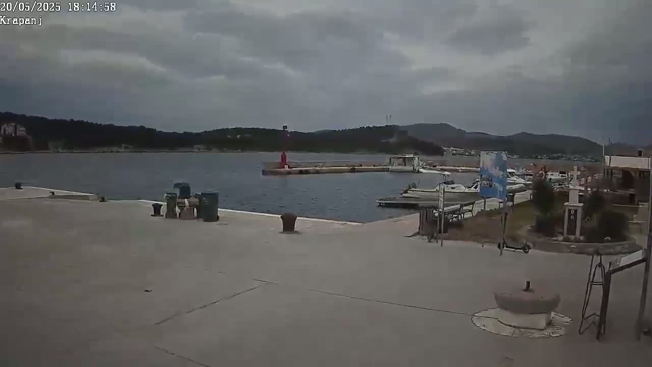 A harbor with several boats is visible on a cloudy day, with a small pier extending into the calm water.