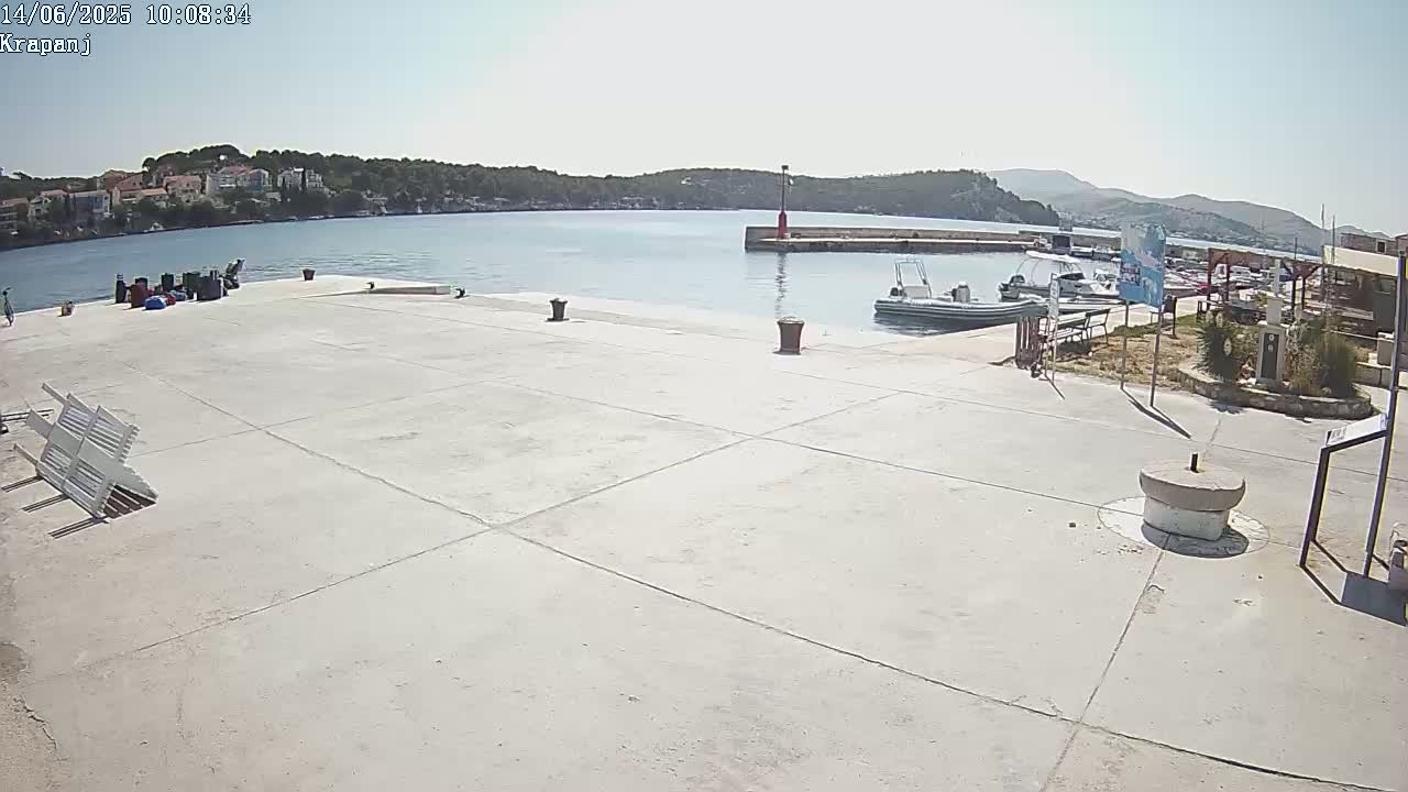A mostly empty concrete dock overlooks a calm bay with several small boats moored nearby under a sunny sky.