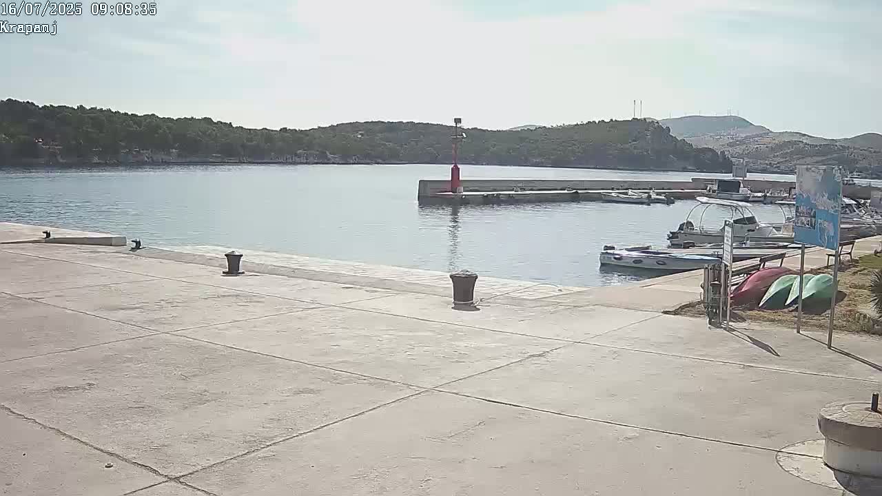 A harbor with several boats docked under a mostly sunny sky, featuring a concrete dock and a small red navigational marker.