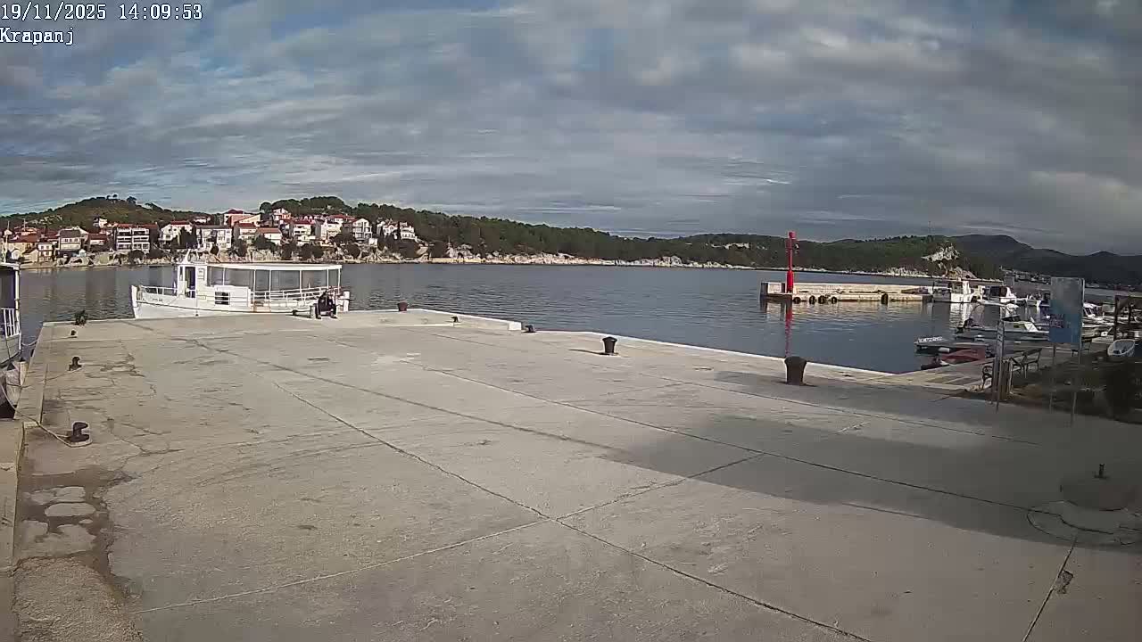A harbor with several boats docked under a mostly sunny sky, featuring a concrete dock and a small red navigational marker.
