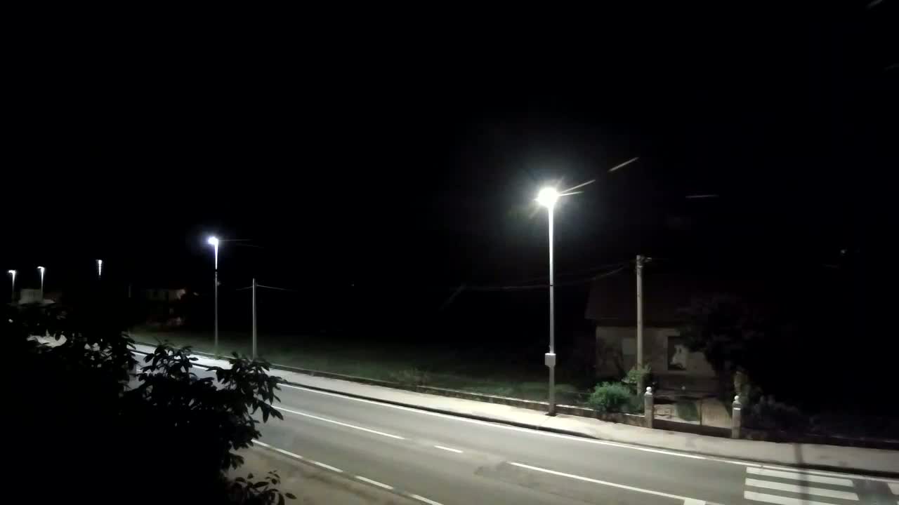 A dark, empty road at night, lit by several streetlights, passes in front of a building and a grassy area.