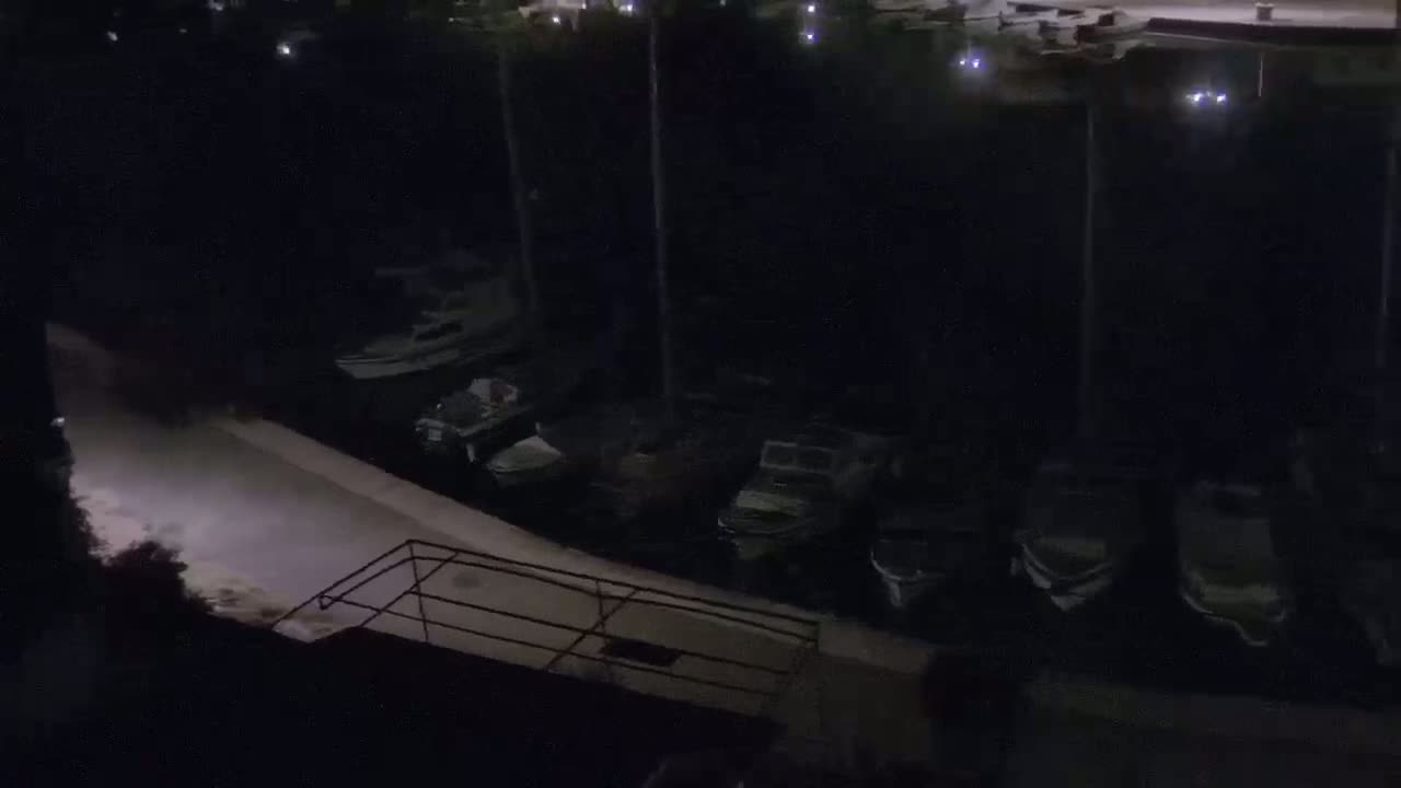 A nighttime view of several boats docked at a marina, under a dark sky.