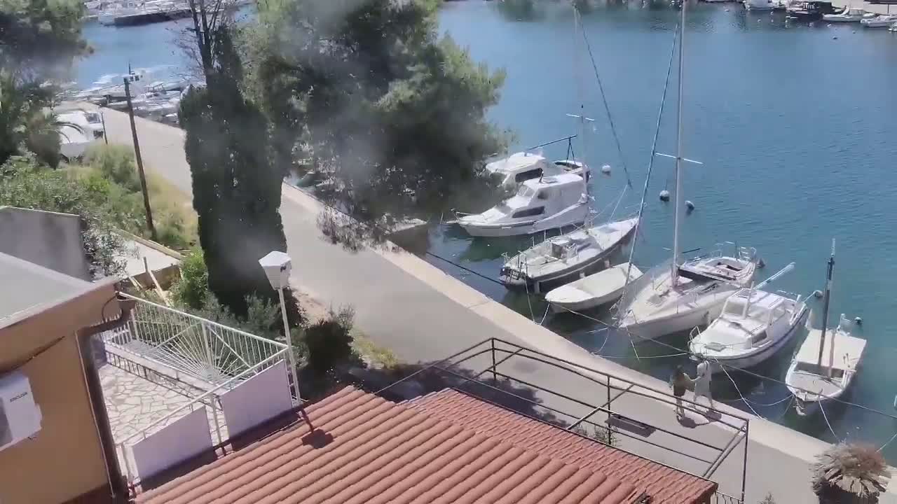 A paved walkway overlooks a calm body of water lined with several docked sailboats and motorboats on a sunny day.