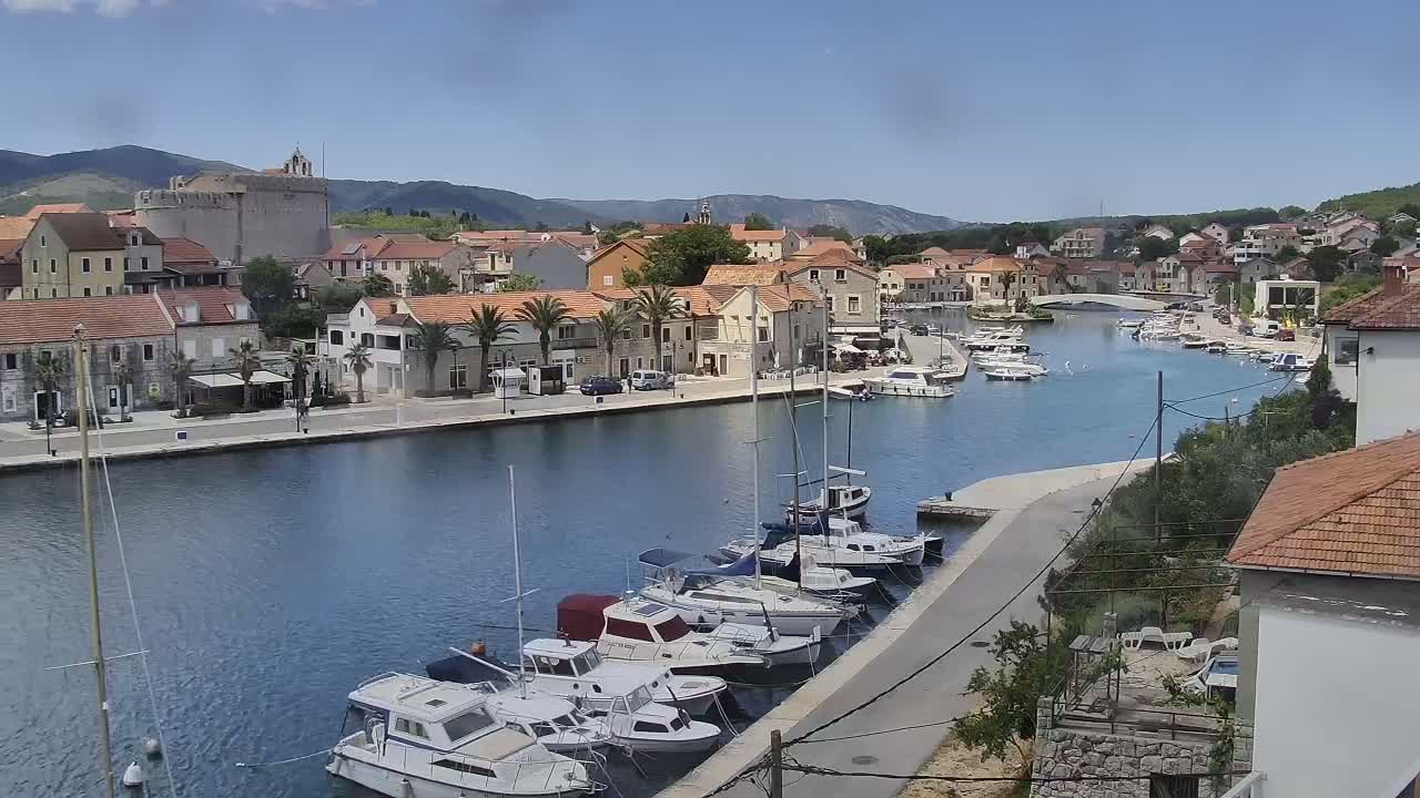 A waterfront town with numerous boats docked in a calm harbor under a sunny sky.
