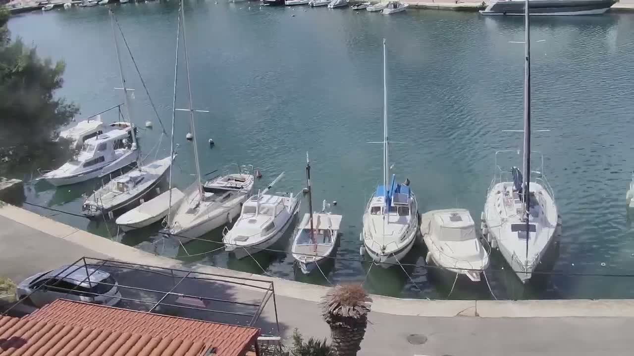 Several sailboats and motorboats are moored in a calm harbor on a sunny day.