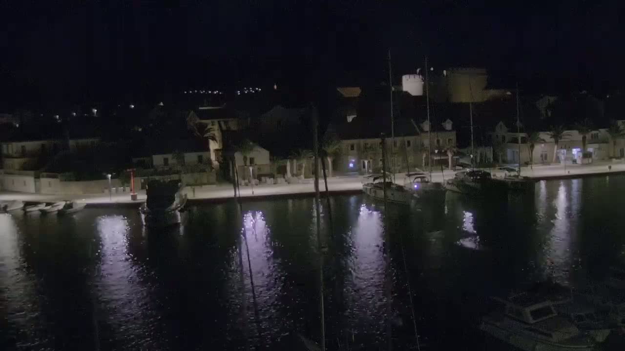 A nighttime view of a calm harbor, lined with buildings and boats, under a clear, dark sky.