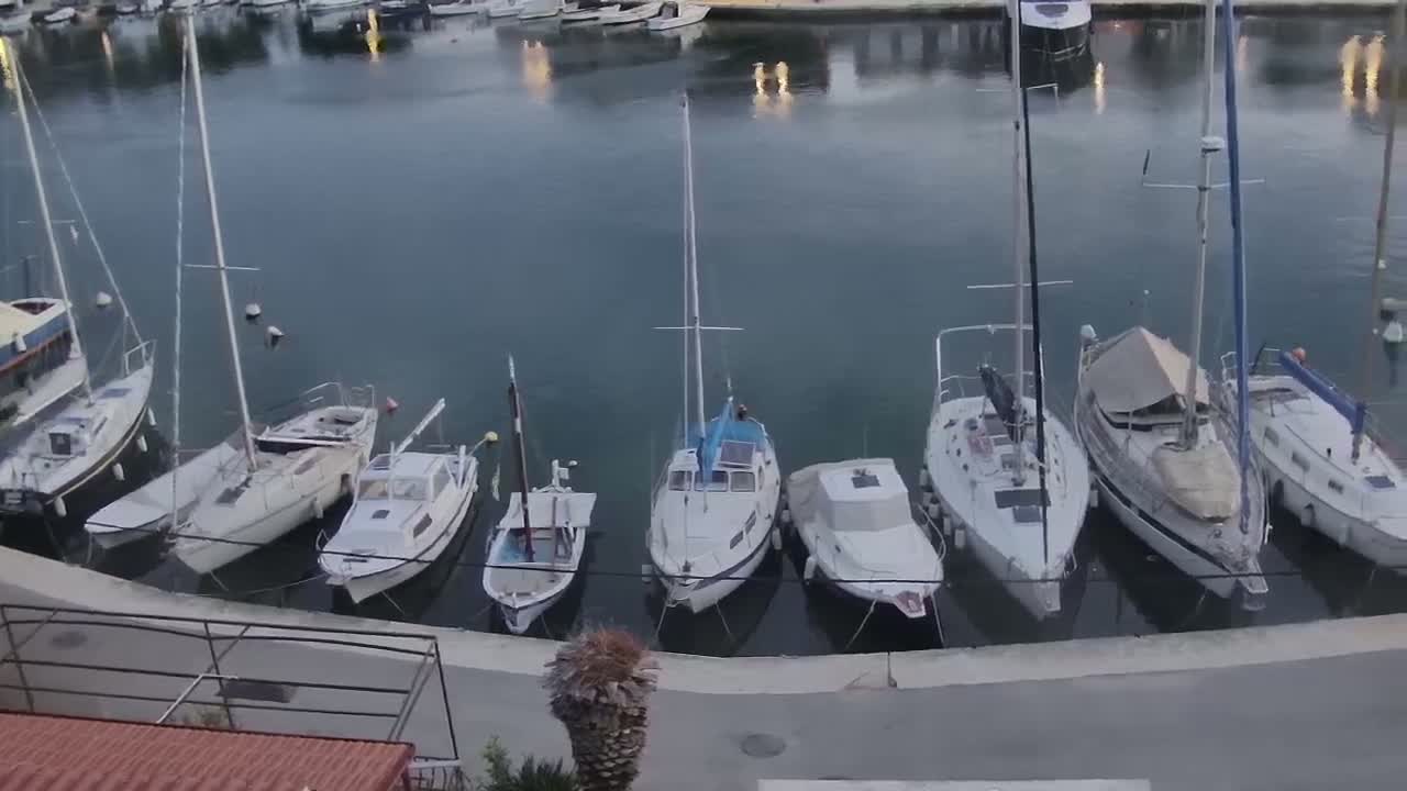 Several sailboats and motorboats are moored in a calm harbor at dusk.