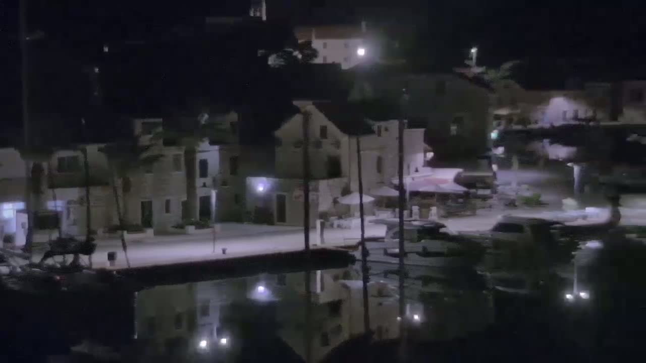 A waterfront village at night, illuminated by streetlights, with calm water reflecting the buildings and boats.