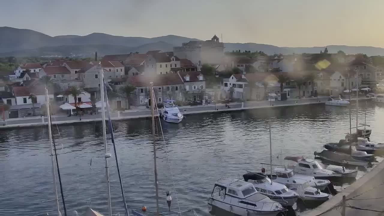 A waterfront town with stone buildings and numerous boats in a calm harbor under an overcast sky.
