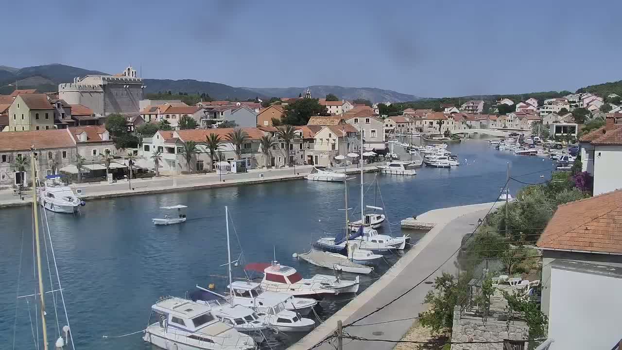A harbor filled with boats is nestled in a town surrounded by mountains under a clear, sunny sky.