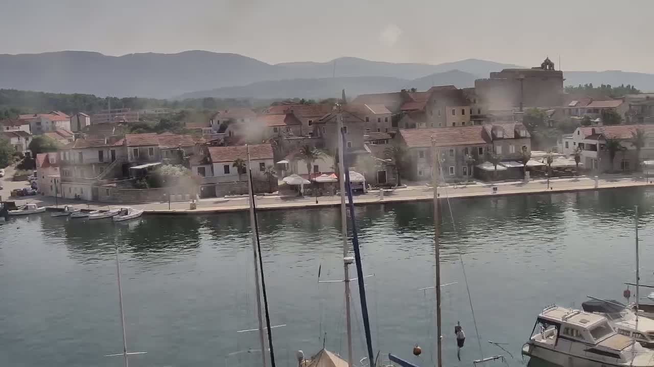 A hazy, sunny day reveals a waterfront town nestled against mountains, with boats moored in a calm harbor.
