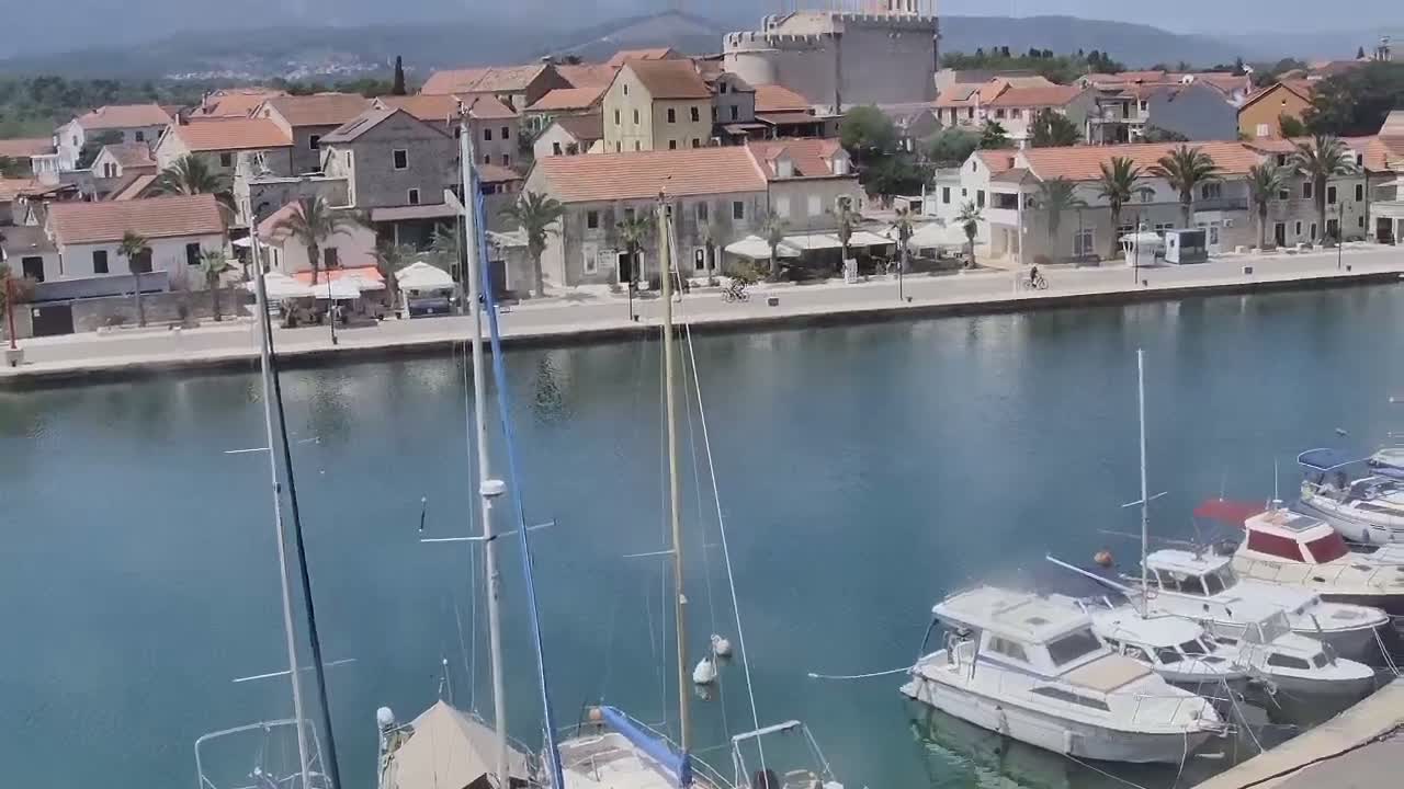 A picturesque waterfront town with calm blue water, several sailboats and motorboats moored in the harbor, and a sunny day.