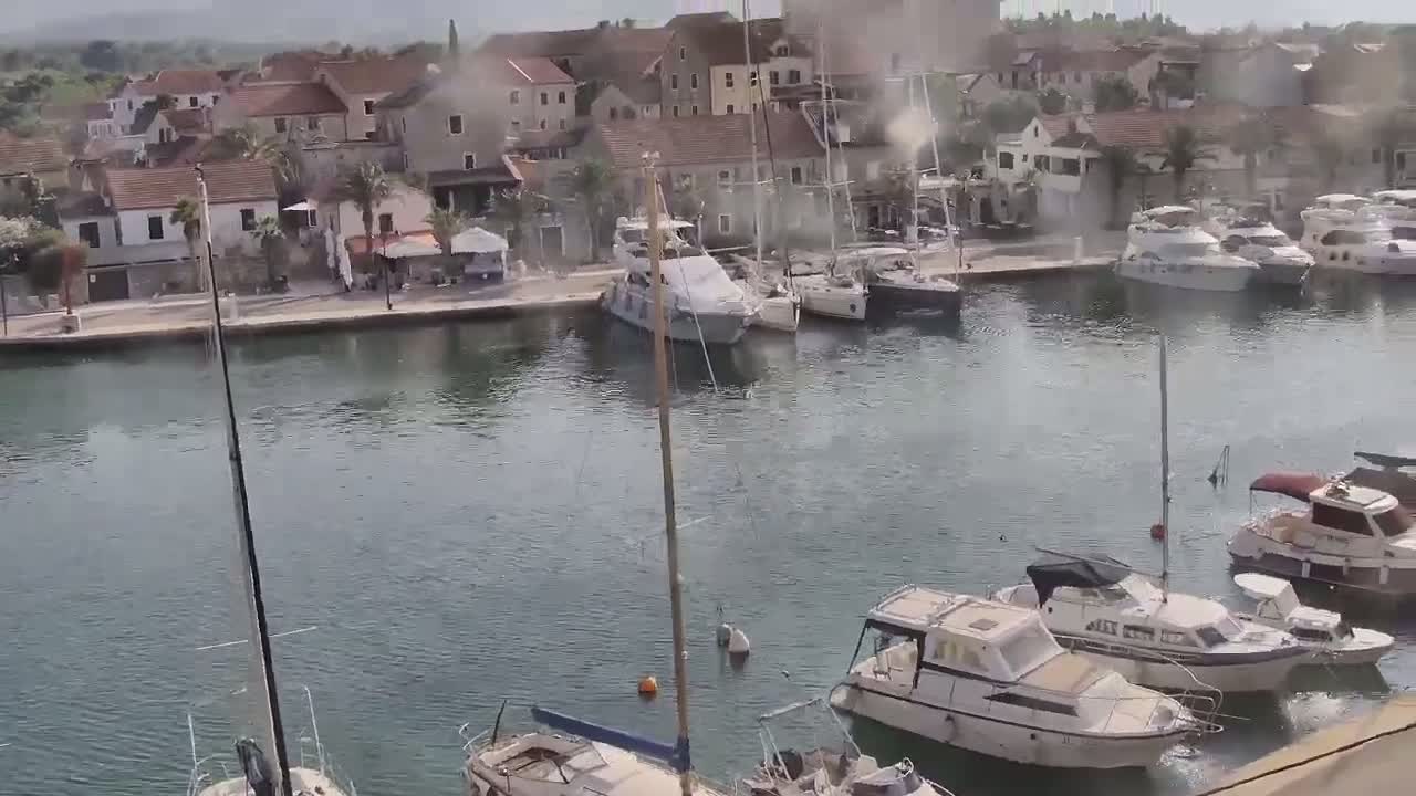 A marina filled with motorboats and sailboats is situated next to a small town on a calm, hazy day.