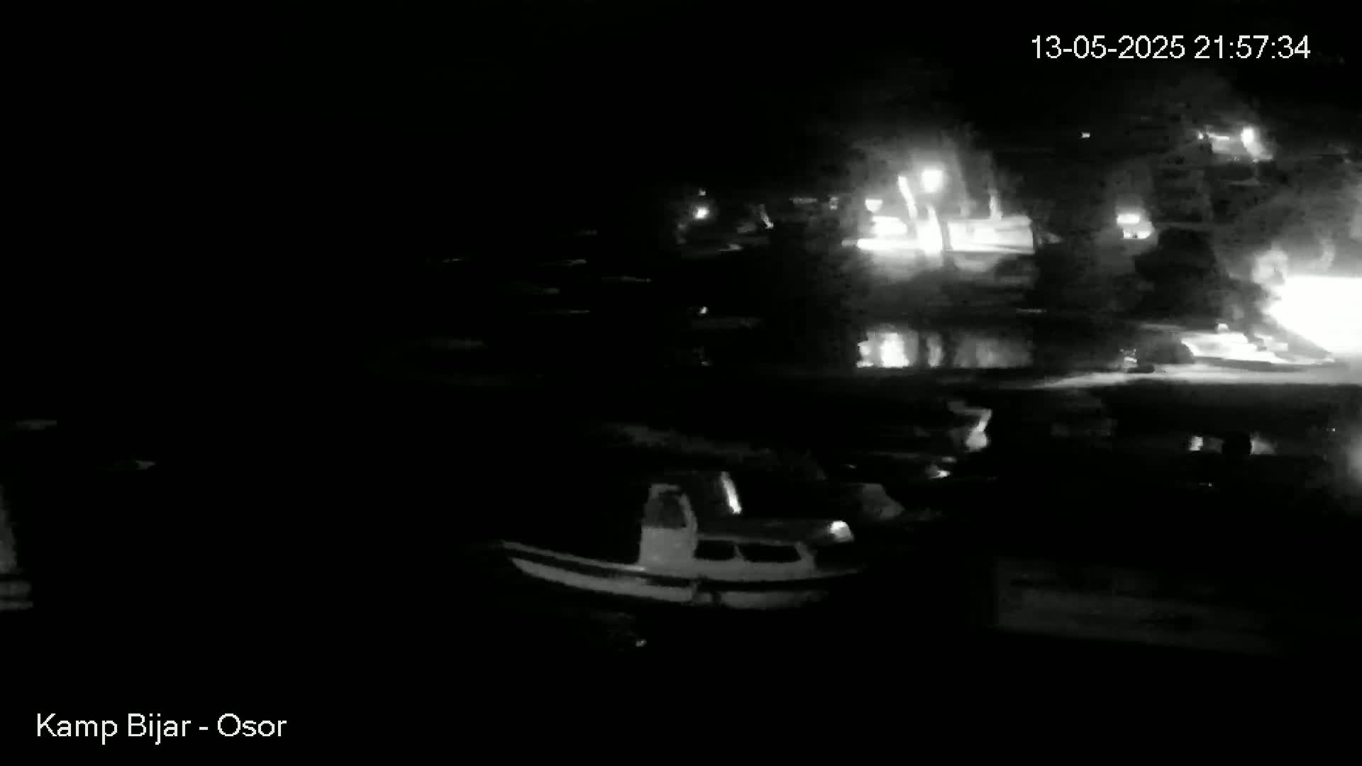 A nighttime, low-light view shows several boats moored at a dock, with faint lights visible in the background.