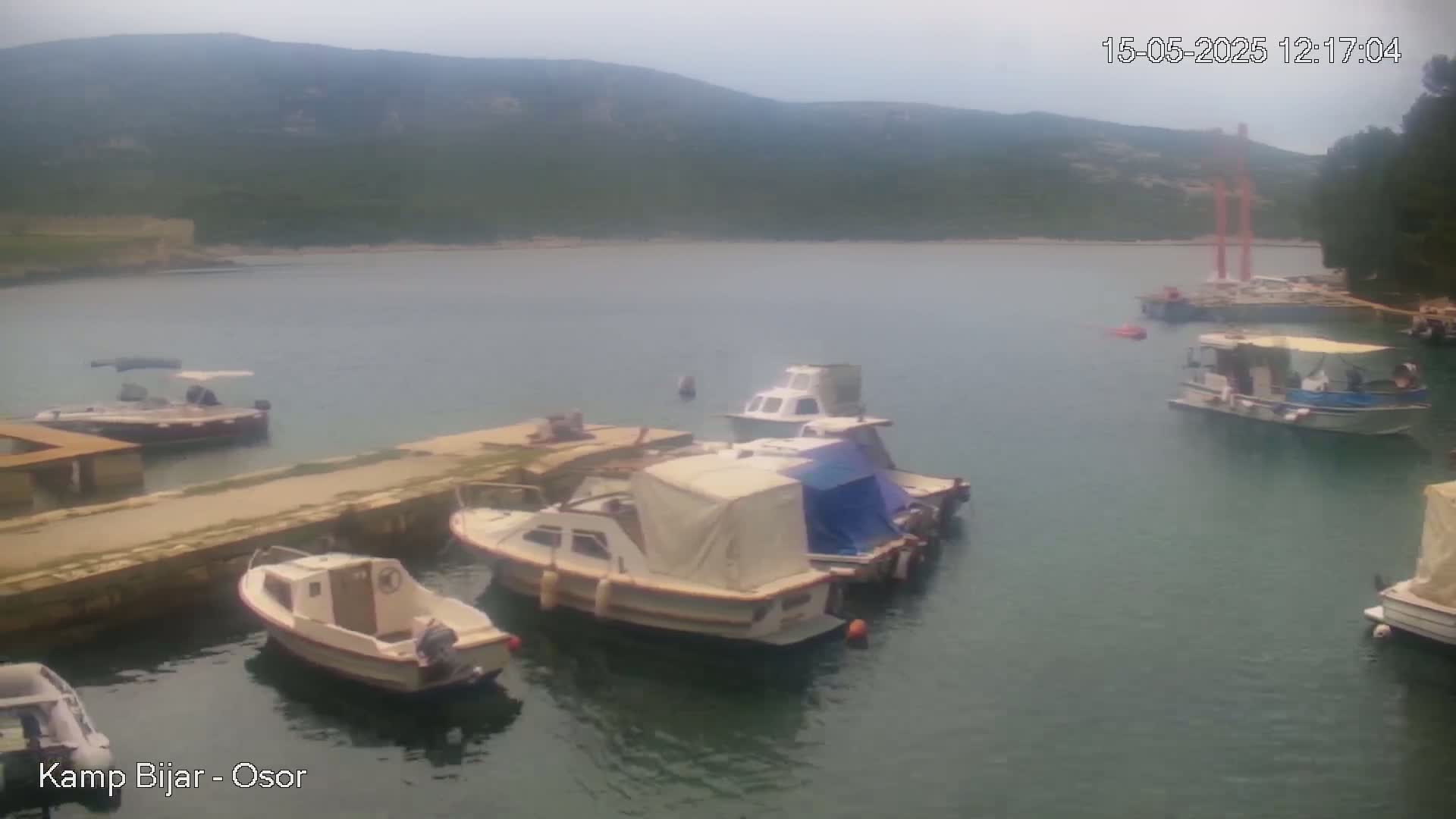 Several small motorboats are moored in a calm bay under an overcast sky, with hills visible in the background.