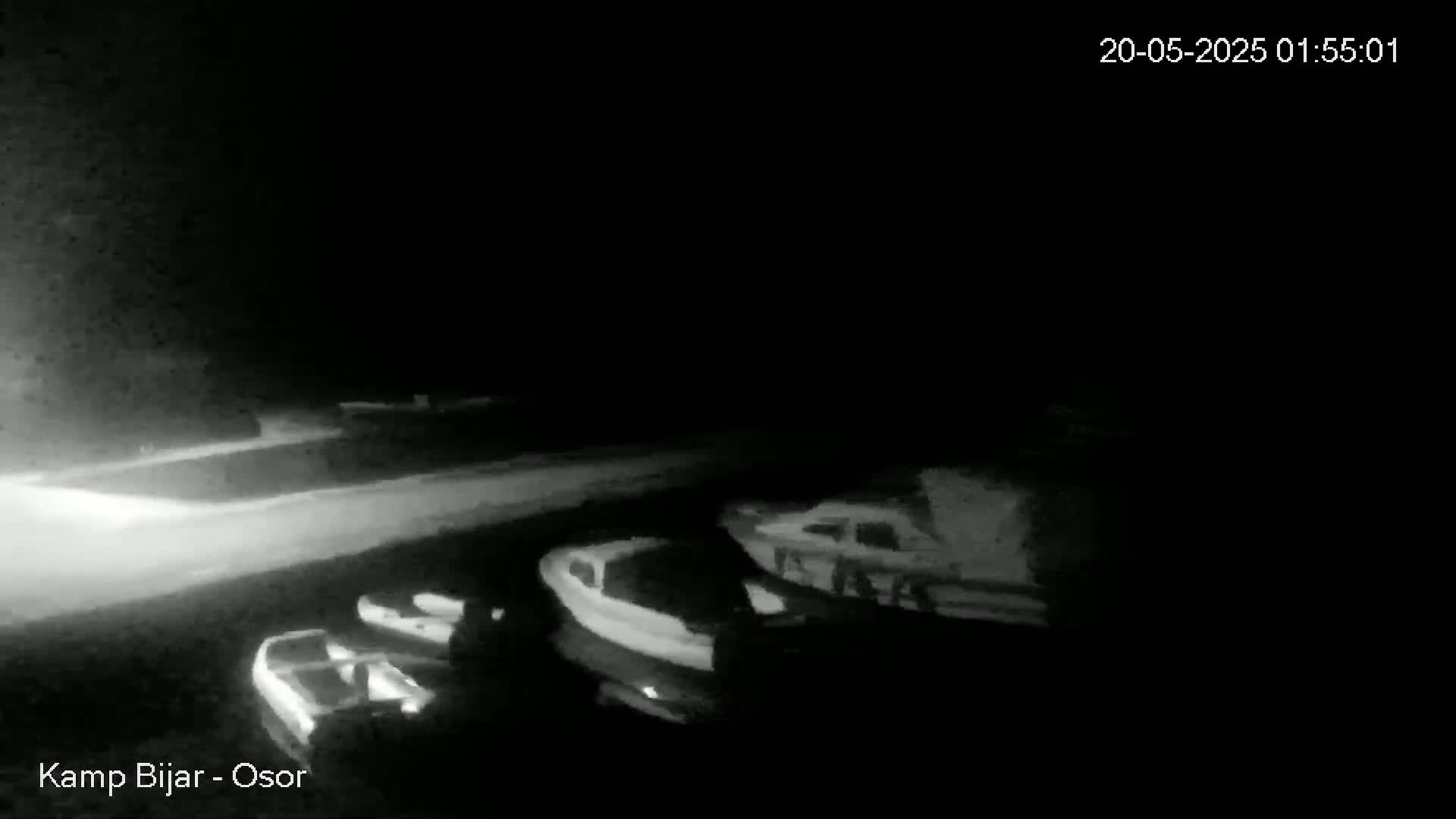 A nighttime, low-light grayscale image shows several boats moored at a dock.