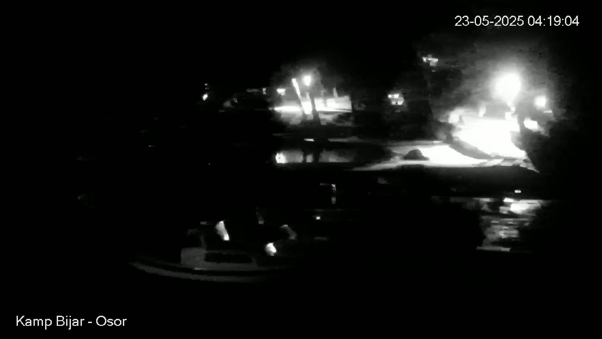 A nighttime, low-light view of a waterfront area with several boats and some illuminated areas nearby.