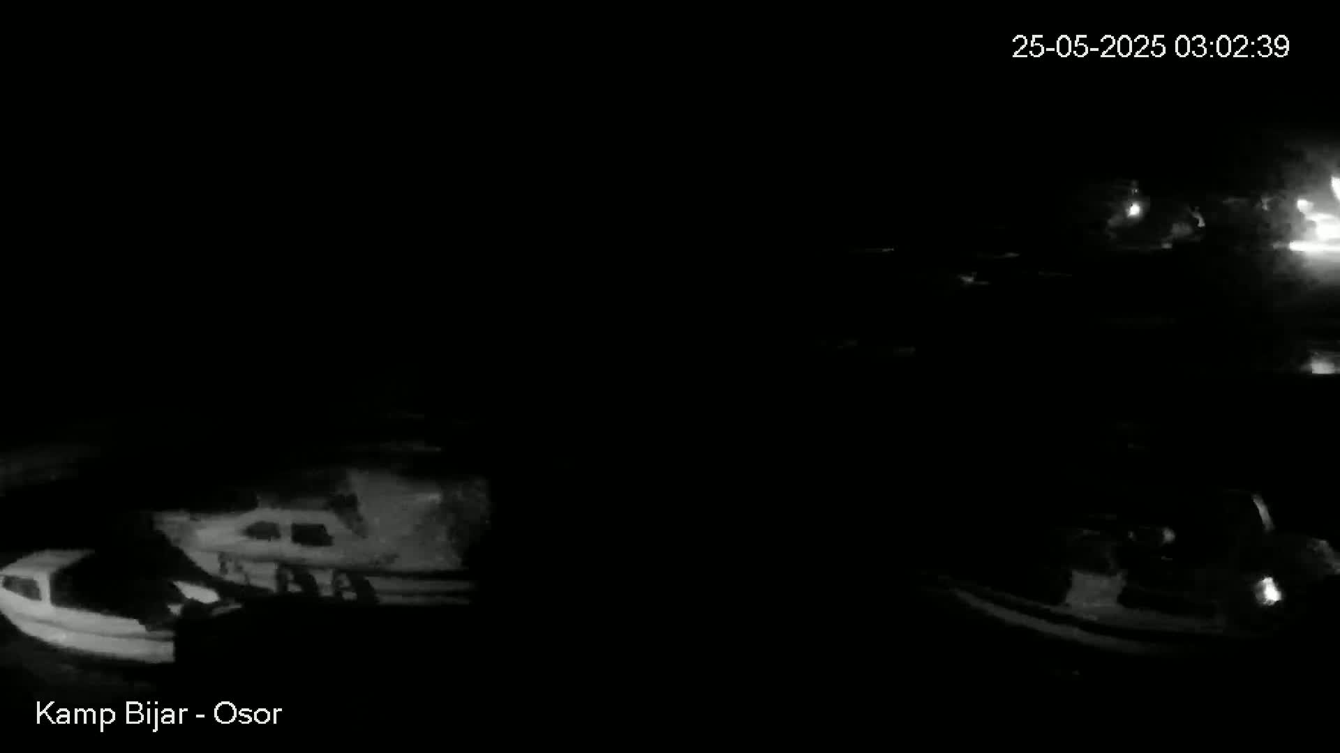 A nighttime, low-light image shows several boats docked at a marina, appearing dark against a black background.