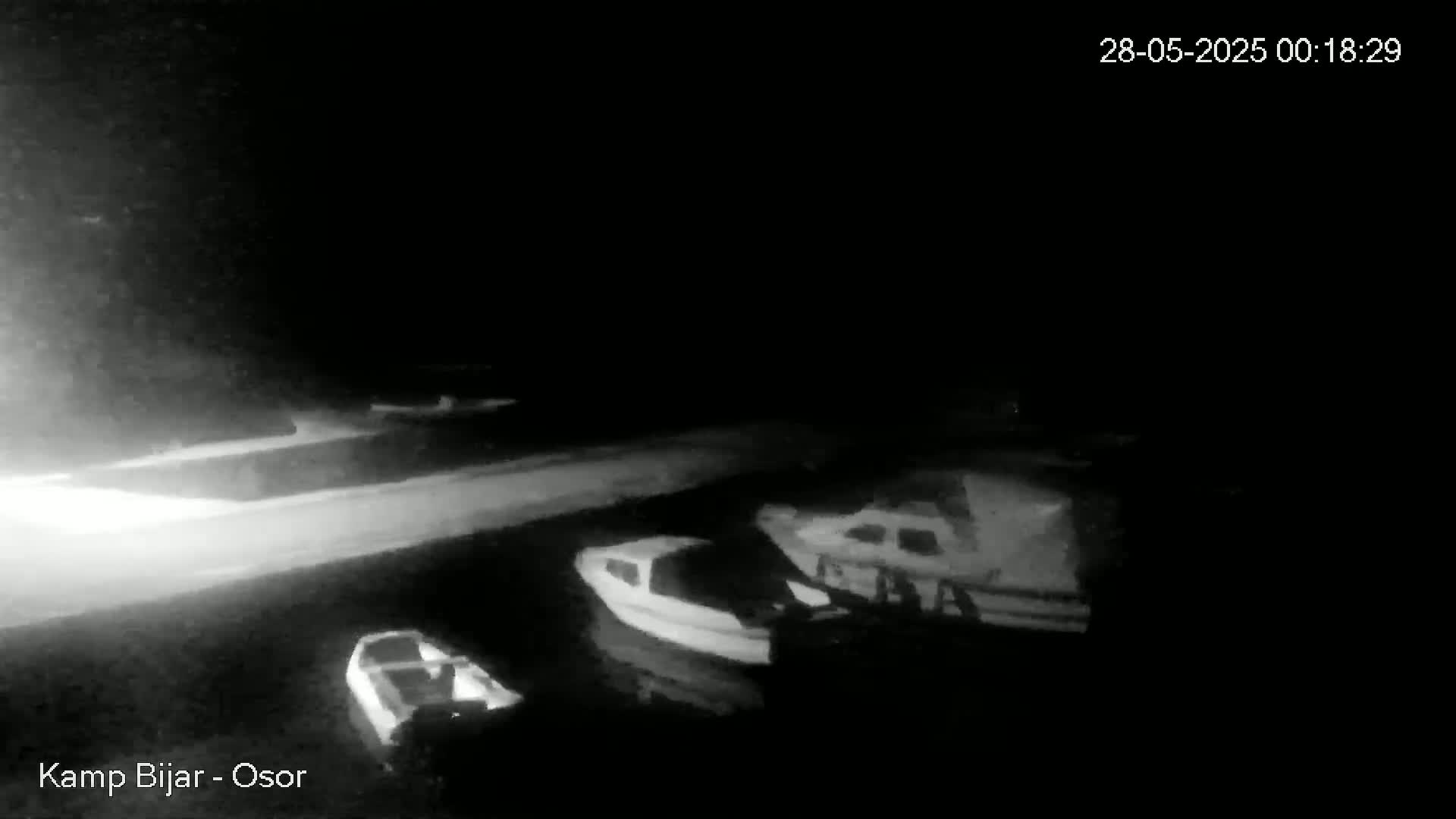 A nighttime, low-light grayscale image shows several small boats moored at a dock.
