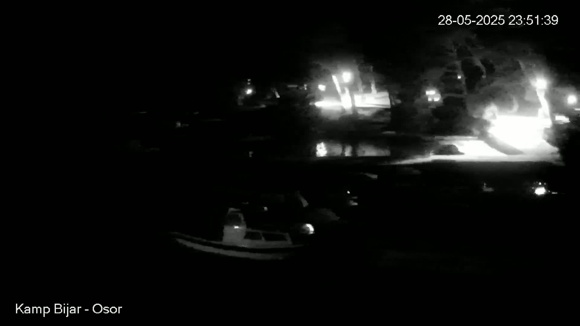A nighttime, low-light view of a marina with several boats moored, illuminated by faint lights from the shore.
