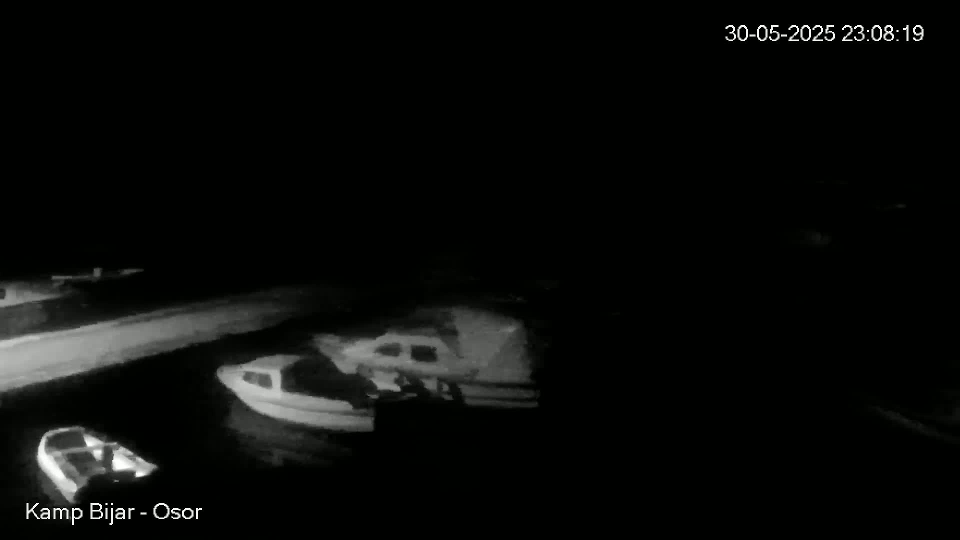 At night, several small boats are moored in dark water near a low wall.