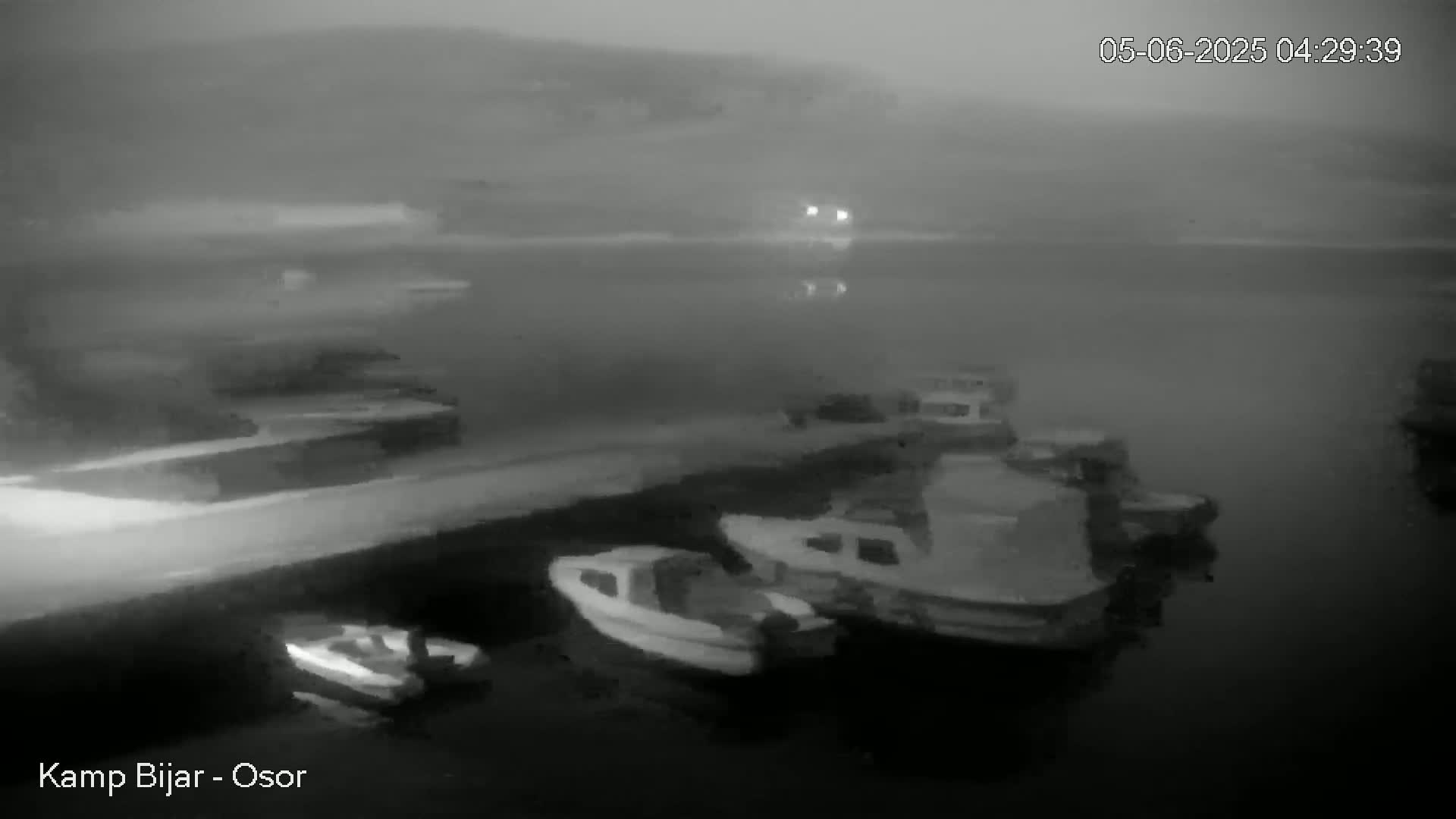 Several small boats are moored at a dock at night in foggy conditions.