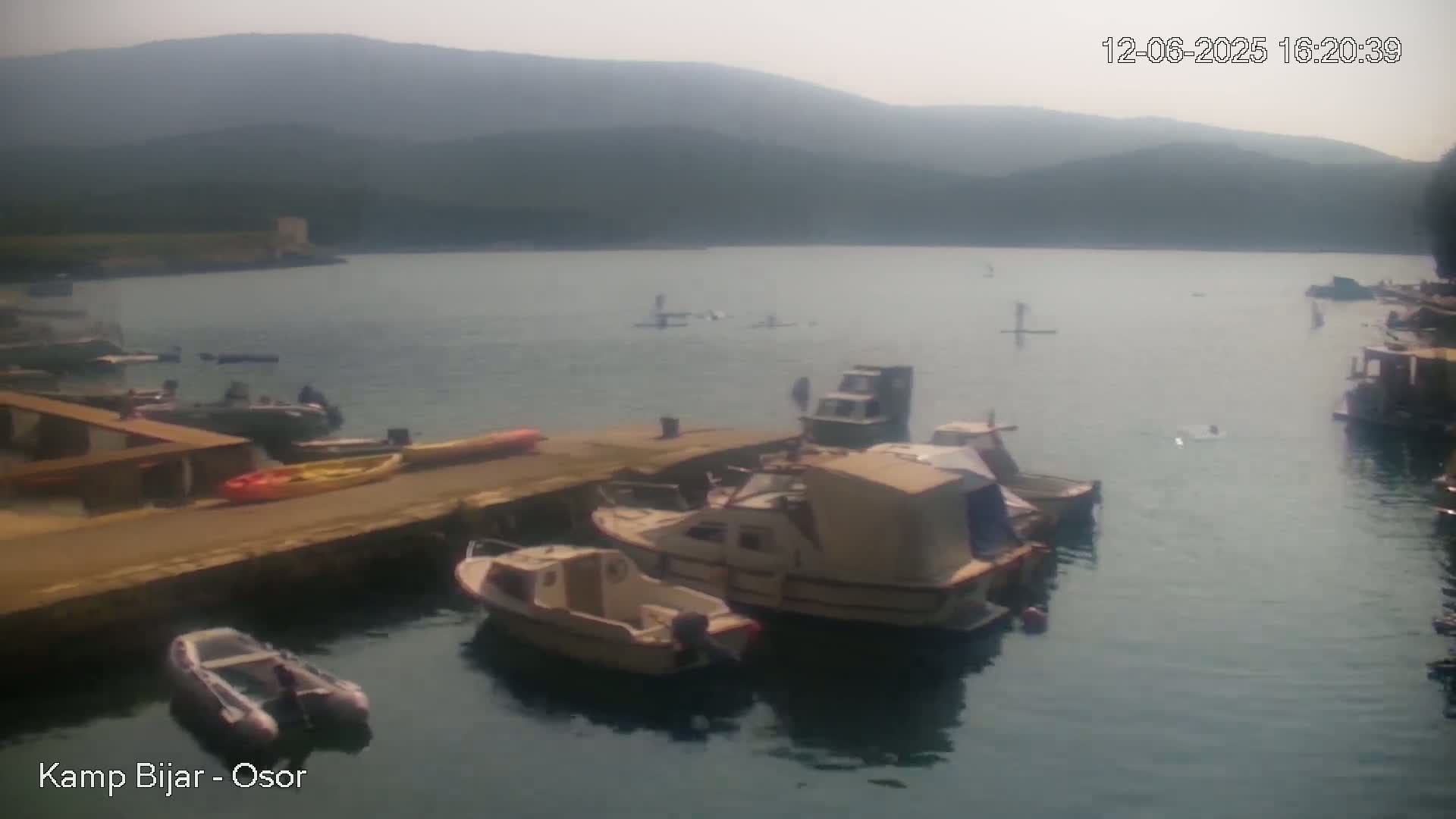 Several boats are moored at a dock on a calm body of water, with hazy mountains in the background.
