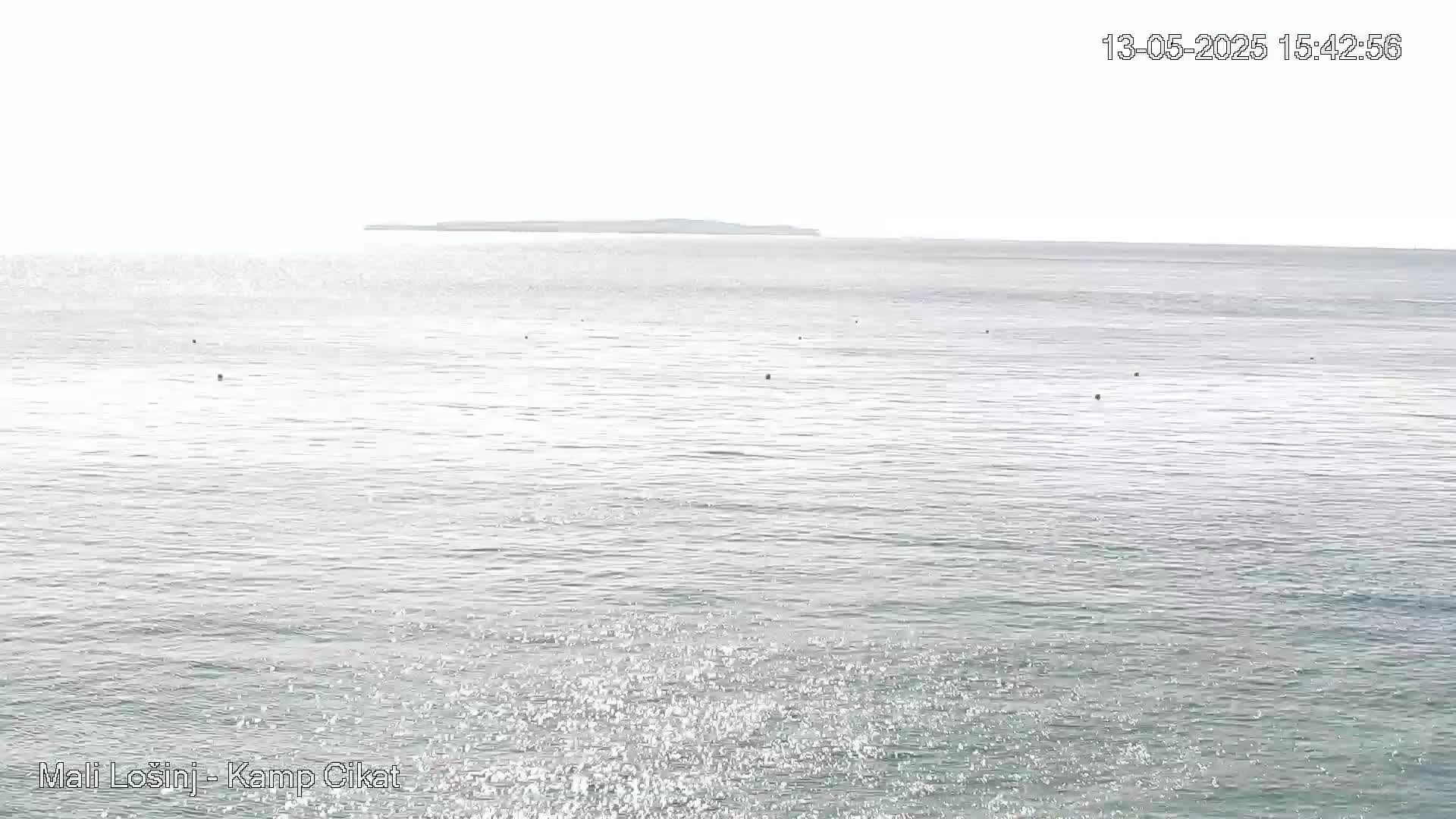A calm, bright sea stretches to a distant, hazy island under a clear sky.