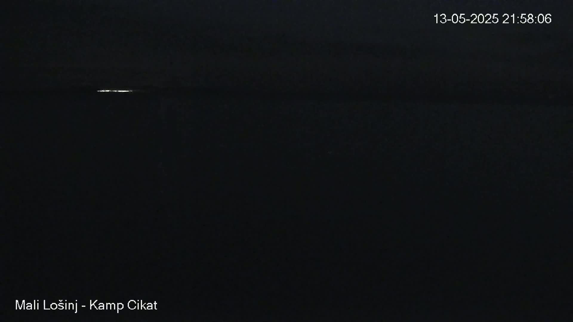 A dark, nighttime scene shows a thin, bright line on the horizon over a mostly black body of water under a dark sky.
