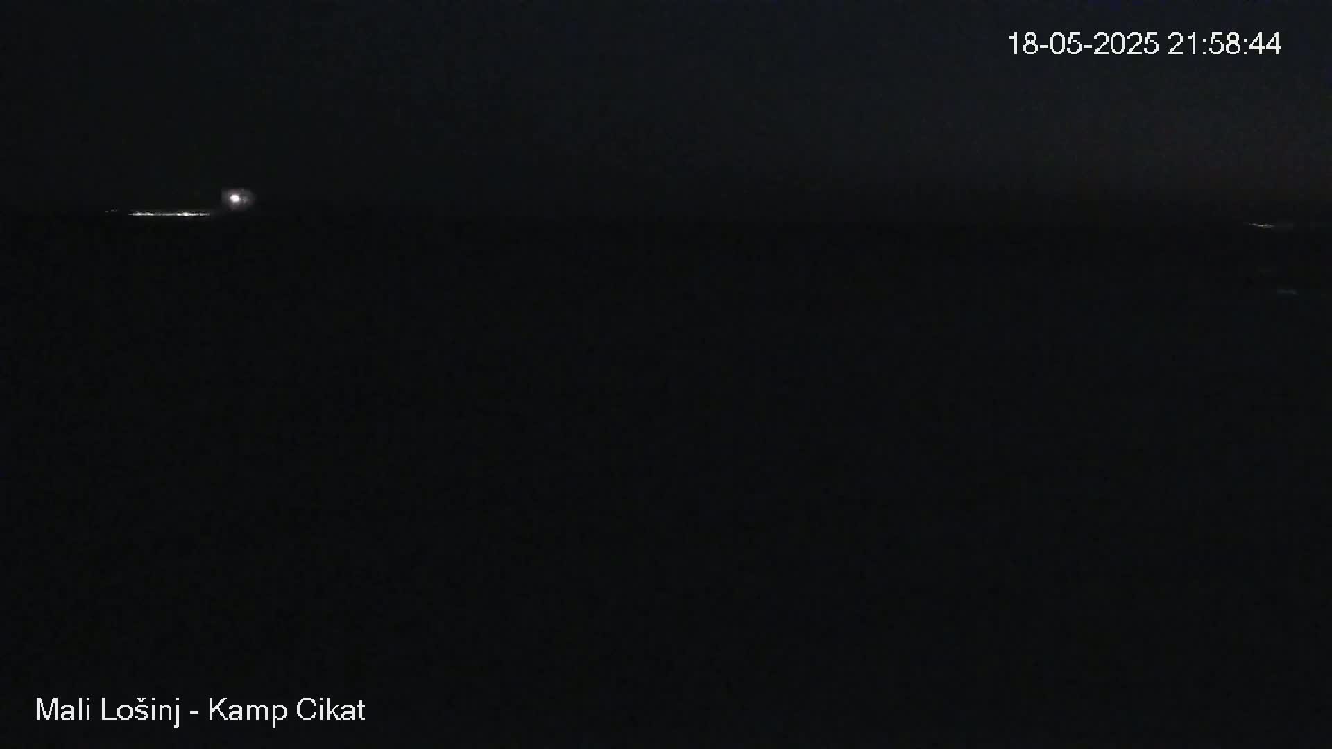 A dark nighttime scene shows a body of water with faint lights on the horizon under a clear, moonlit sky.