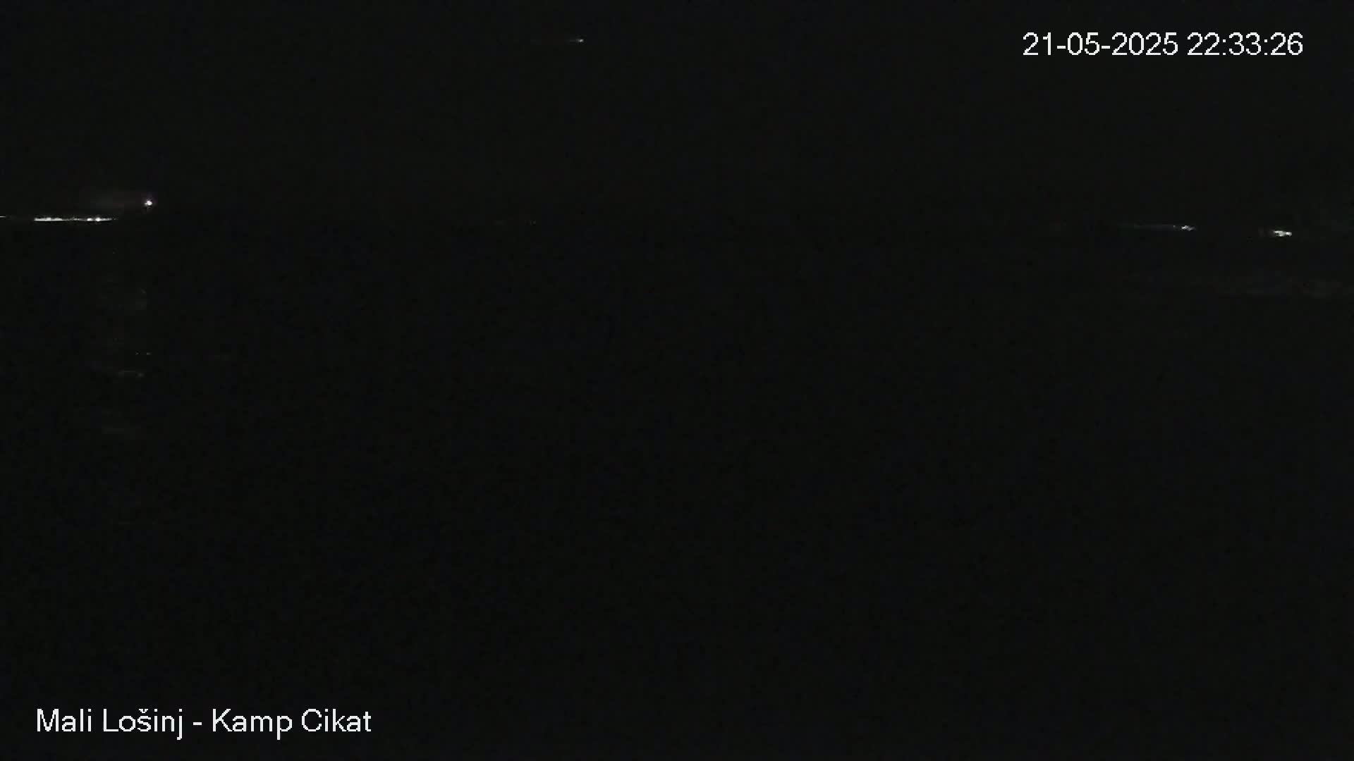 A dark nighttime scene shows a faint horizon line with a few distant lights, under a clear sky.