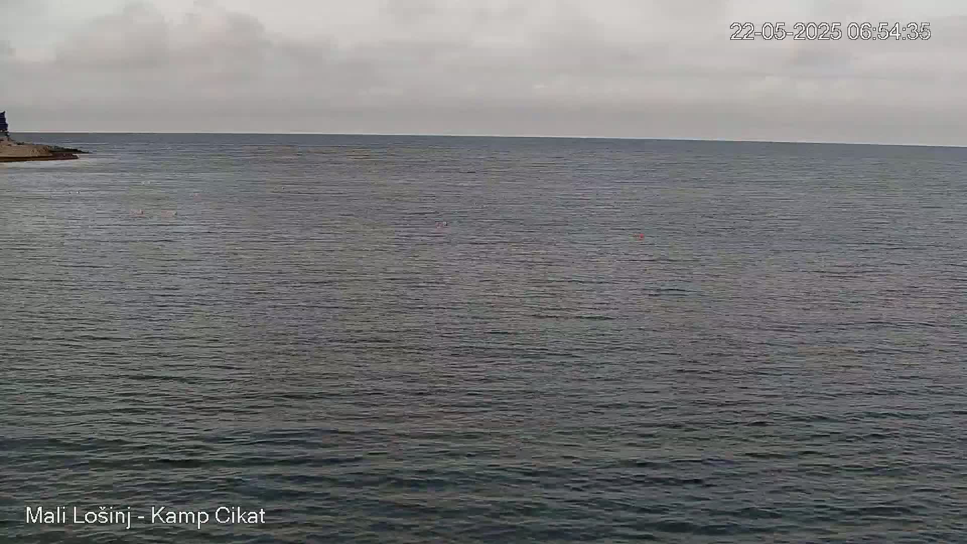 A calm, gray-sky day over dark-grey water shows a distant shoreline with a small structure.