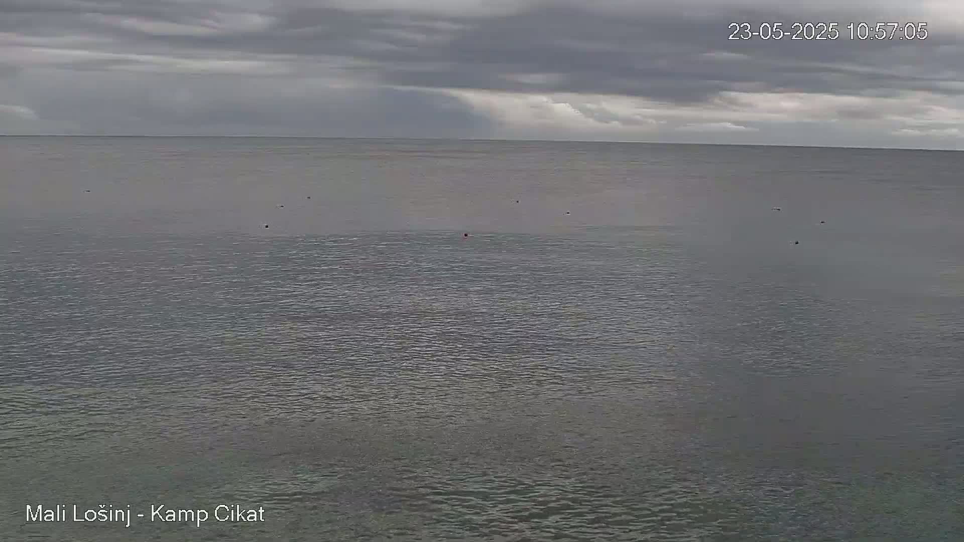 A mostly cloudy sky hangs over a calm, gray-blue sea with a few small objects scattered across its surface.