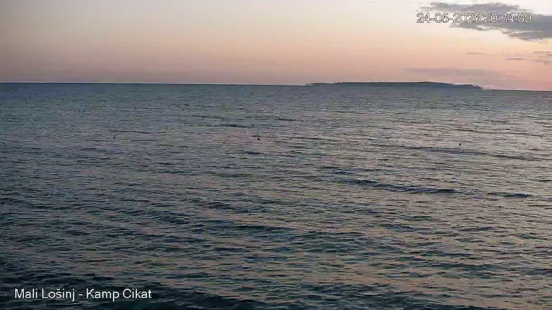 A calm sea under a pale pink and dusky sunset shows a distant island on the horizon.
